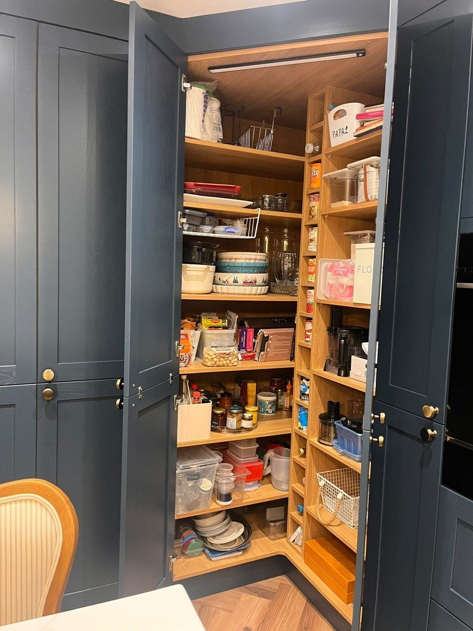 Corner larder cupboard opened to show oak-effect shelving